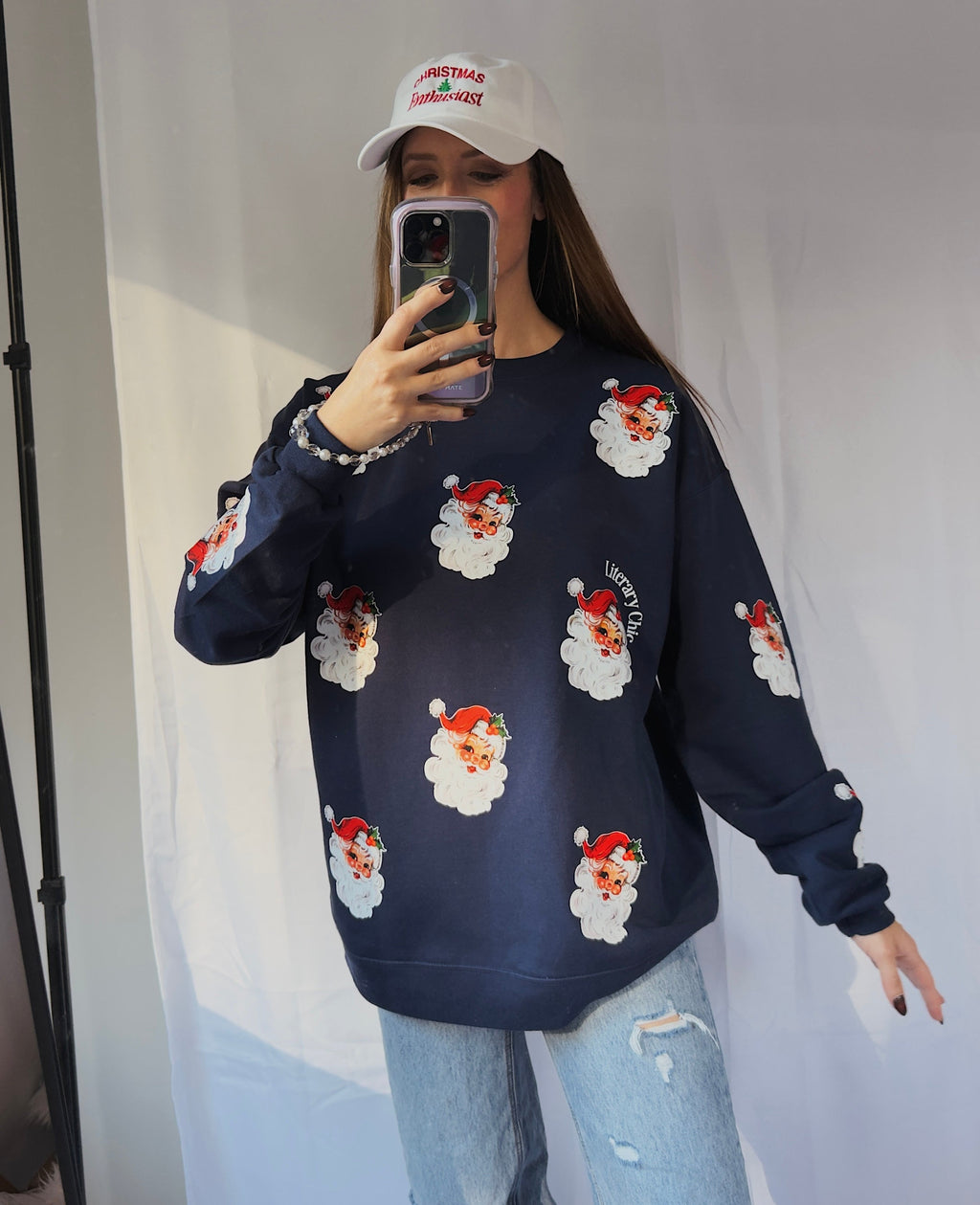 Person wearing a navy blue sweater with Santa Claus prints and light blue jeans, taking a mirror selfie.