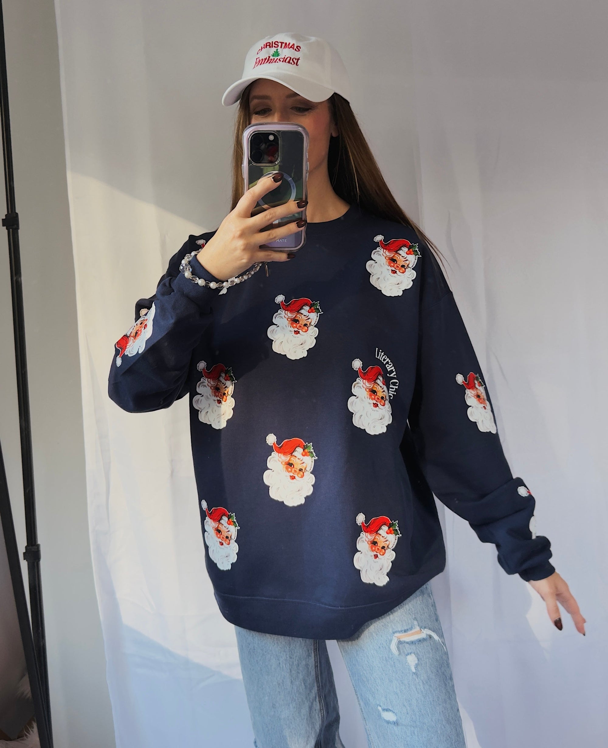 Person wearing a navy blue sweater with Santa Claus prints and light blue jeans, taking a mirror selfie.