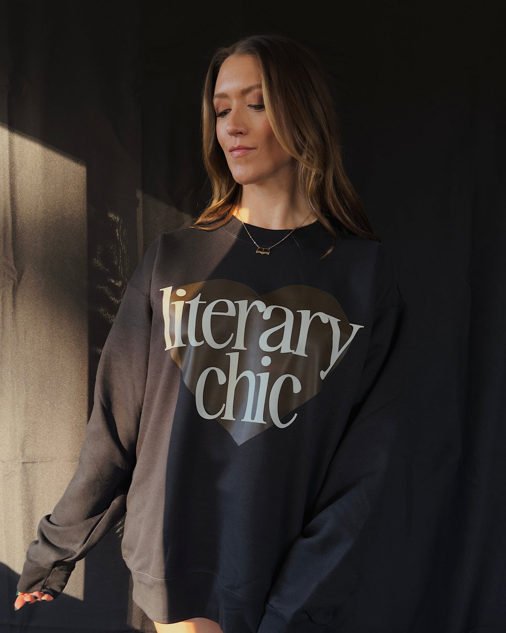 Woman wearing a black sweatshirt with 'literary chic' text against a dark background